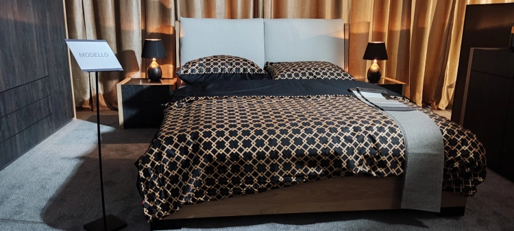 Łóżko MODELO z tapicerowanym zagłówkiem New Elegance. Łóżko z miękkimi poduchami na odchylonym wezgłowiu, w tkaninie Positano o strukturze delikatnej plecionki z kolekcji Davisa.