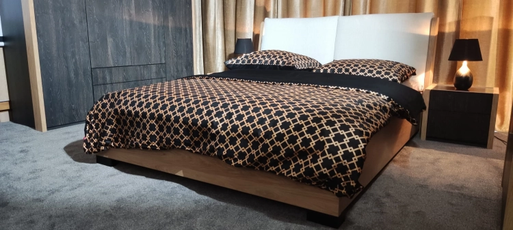 Łóżko MODELLO z tapicerowanym zagłówkiem New Elegance. Łóżko z miękkimi poduchami na odchylonym wezgłowiu, w tkaninie Positano o strukturze delikatnej plecionki z kolekcji Davisa.