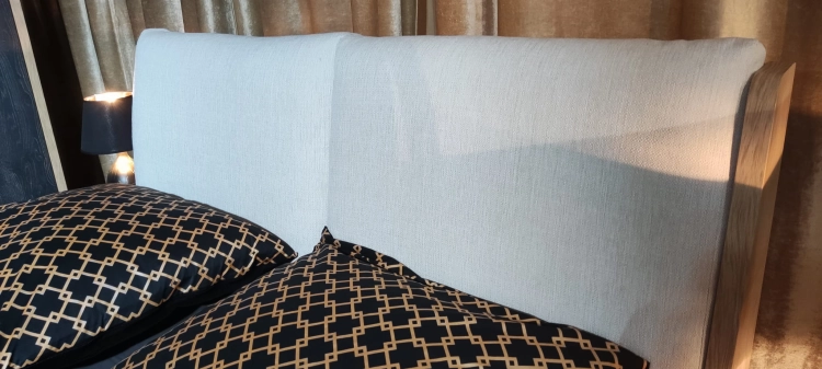 Łóżko MODELLO z tapicerowanym zagłówkiem New Elegance. Łóżko z miękkimi poduchami na odchylonym wezgłowiu, w tkaninie Positano o strukturze delikatnej plecionki z kolekcji Davisa.