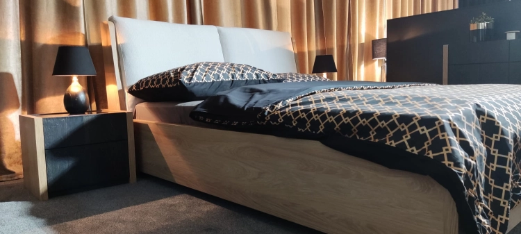 Łóżko MODELLO z tapicerowanym zagłówkiem New Elegance. Łóżko z miękkimi poduchami na odchylonym wezgłowiu, w tkaninie Positano o strukturze delikatnej plecionki z kolekcji Davisa.